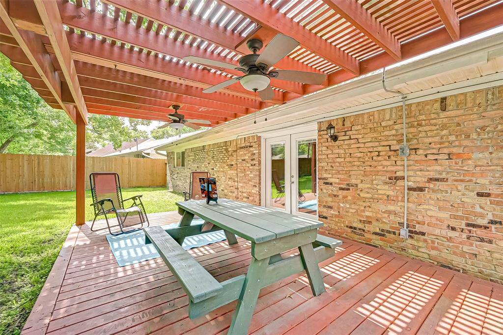 The backyard has covered patio with two ceiling fans and picnic table of outdoor grilling.