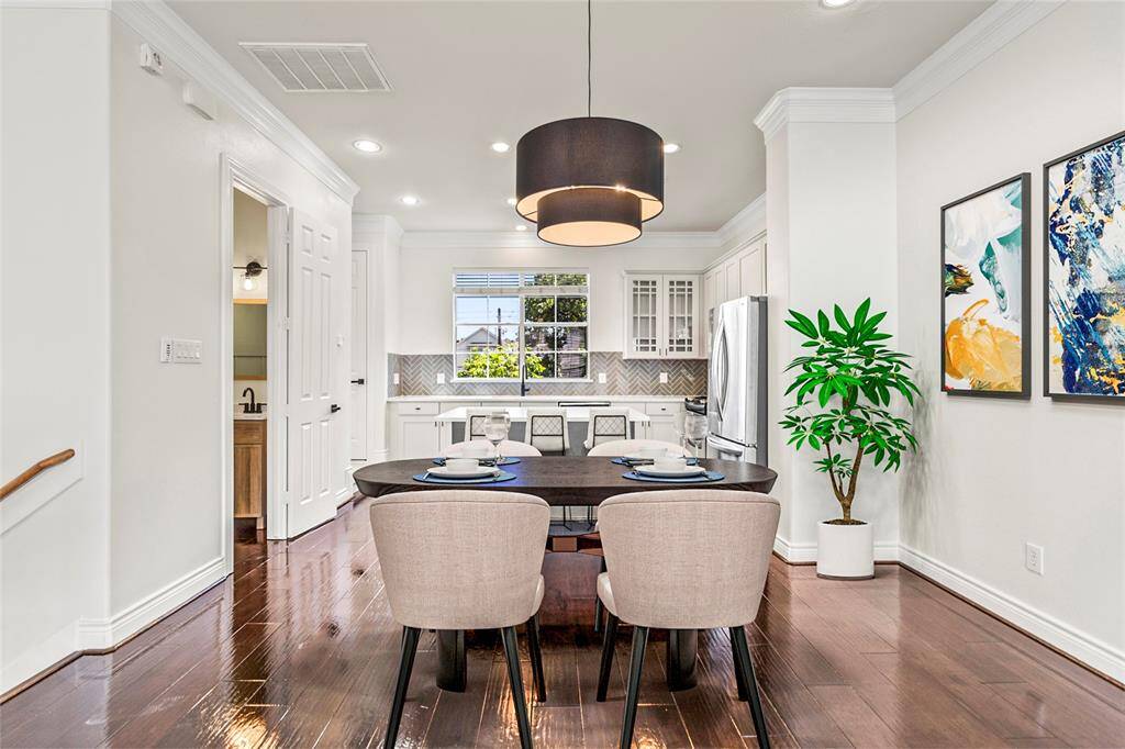 Your open-concept living flows seamlessly from the kitchen to your dining area, where a bold, modern light fixture makes a stylish statement. Rich hardwood floors reflect the natural light pouring in, creating a warm and polished feel throughout. Whether hosting dinner or enjoying quiet evenings in, this space sets the tone for versatile, comfortable living.