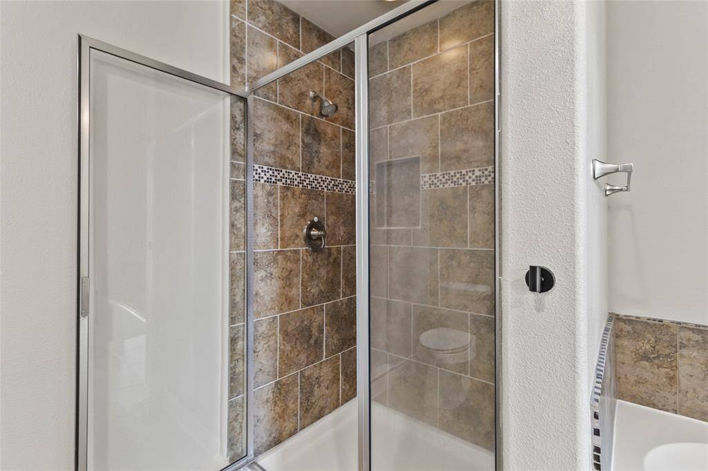 The glass-enclosed walk-in shower features rich tilework with a mosaic accent strip and built-in niche, adding both style and function to your en-suite retreat. It’s a clean, modern space designed for daily ease.