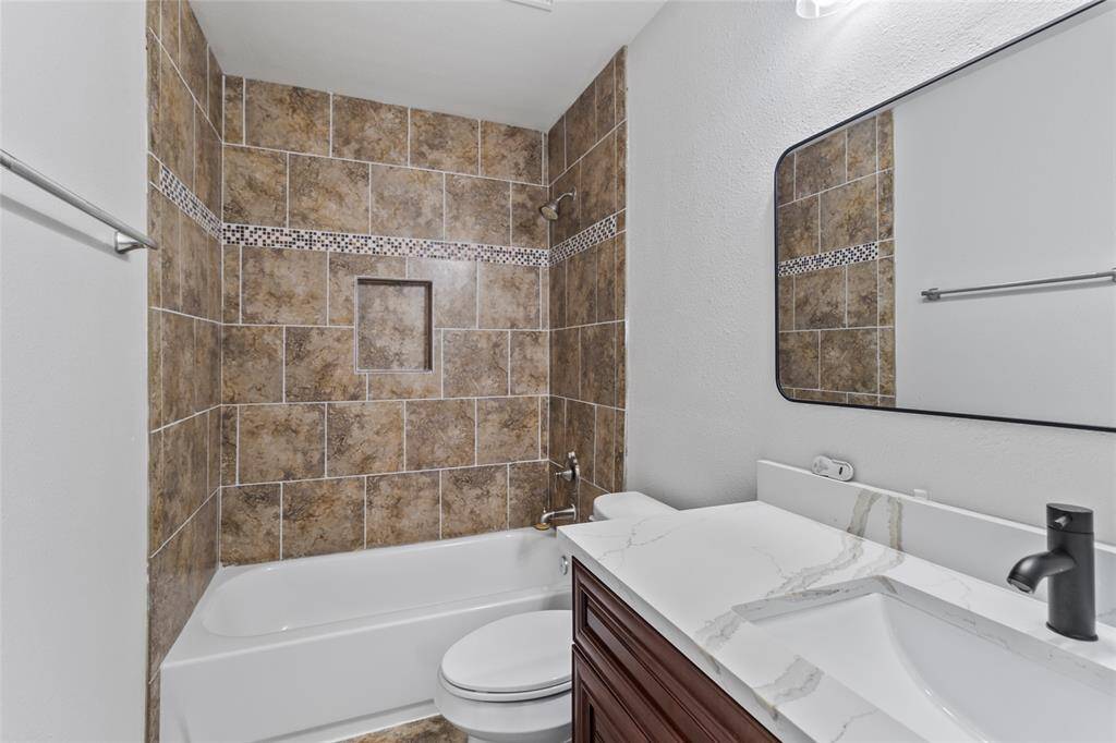 Modern touches and timeless finishes come together in your full bath, featuring a rich wood vanity with marble-style countertop, matte black fixtures, and a tiled tub-shower combo with mosaic accents and a built-in niche for added function.