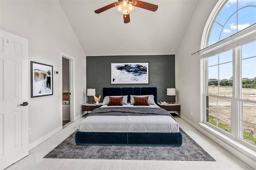 A vaulted ceiling and oversized arched window give your primary suite an open, airy feel with plenty of natural light. The dark accent wall adds a bold touch of contrast while maintaining a calm, restful atmosphere.