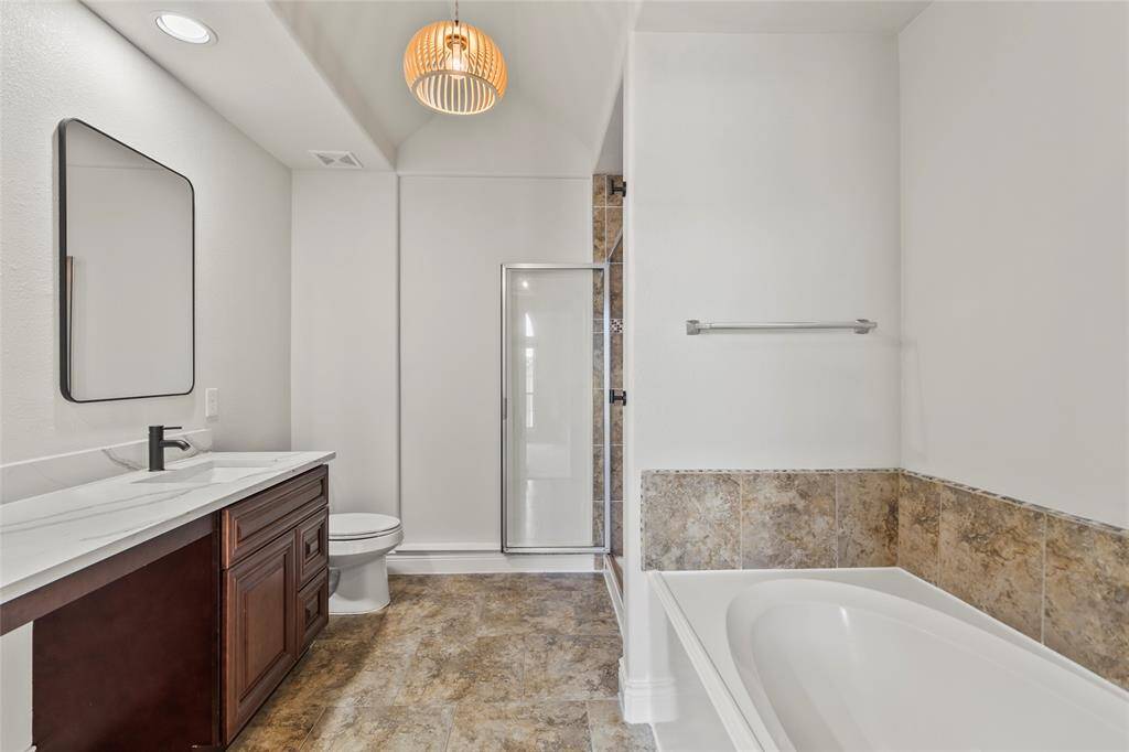 Your en-suite bath combines style and comfort with a deep soaking tub, separate glass-enclosed shower, and dual-sink vanity topped with marble-look counters. Tile flooring and warm finishes add a timeless touch to your daily routine.