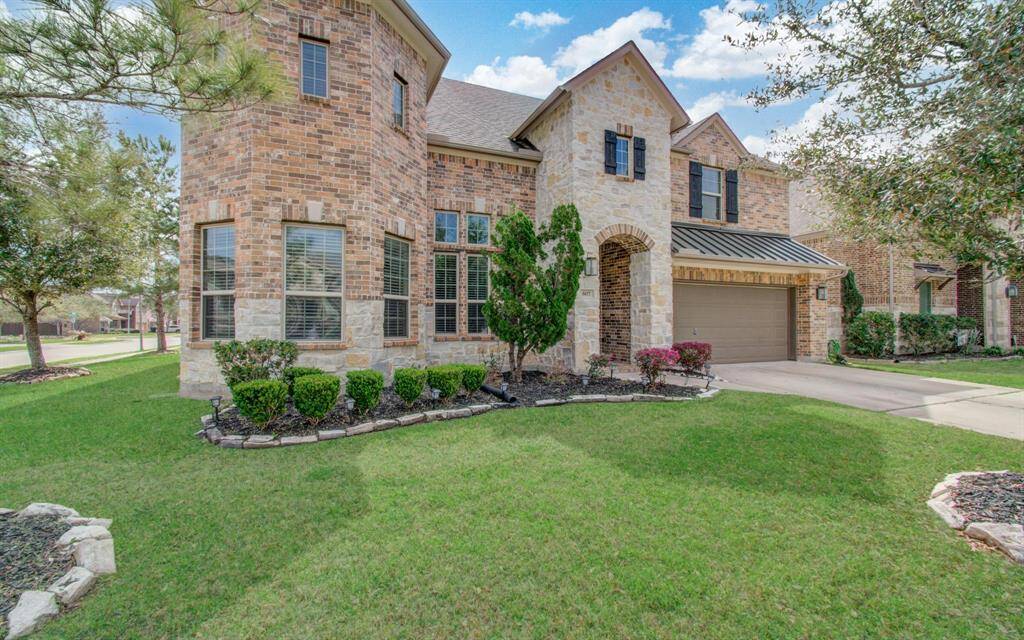 This charming two-story brick home features a well-maintained front yard with lush greenery and manicured shrubs. It includes a two-car garage and a welcoming arched entryway, offering great curb appeal in a suburban neighborhood setting.