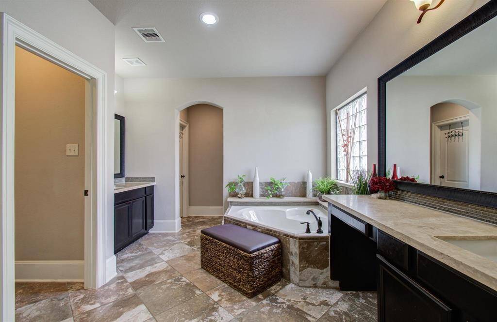 This spacious bathroom features elegant tile flooring, a large soaking tub, dual sink vanities with dark cabinetry, and a bright window for natural light. Cozy and functional, it provides ample storage and a relaxing atmosphere.