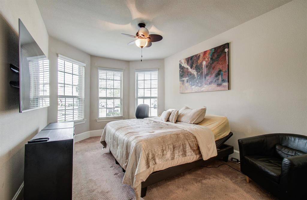 This secondary bedroom downstairs features a bay window for ample natural light, a ceiling fan, neutral walls, and carpeted flooring. It includes an ensuite bath with a shower.