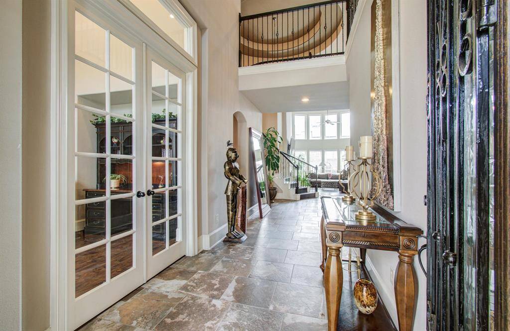 This elegant home entryway features high ceilings and abundant natural light. It includes a grand staircase and stylish tile flooring. French doors lead into a cozy office space, adding to the inviting atmosphere.
