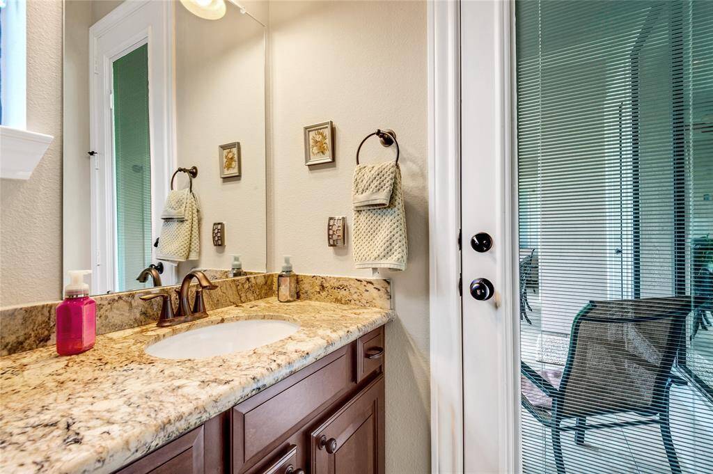The  first floor guest bathroom features a modern glass-enclosed shower with elegant tile work, a stylish vessel sink on a granite countertop, and rich wooden cabinetry. It can also a powder room.