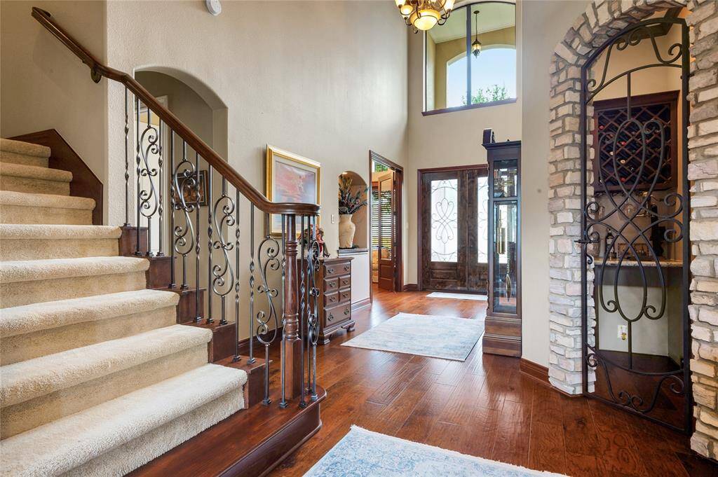 This elegant entryway features a grand staircase with ornate iron and wood railings, rich hardwood flooring, and a high ceiling. A stone archway leads to a cozy nook, with a clear story window.