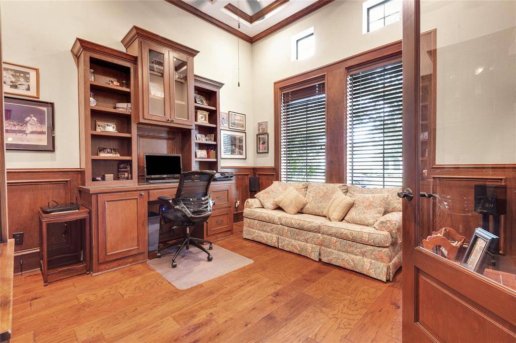 The study showcases  warm wood paneling and built-in library shelving. Multi level ceiling with crown molding.