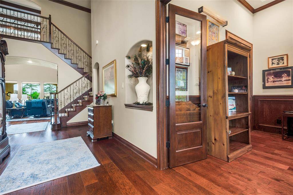 This welcoming entryway features rich hardwood floors, an elegant staircase with wrought iron railing, and a cozy reading nook with built-in shelving. The space transitions seamlessly into a bright, open living area with large windows.