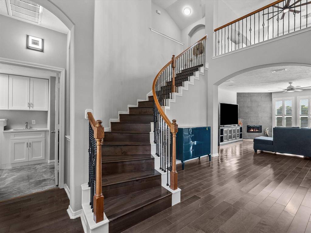 Elegant curved staircase with rich wood accents and wrought iron balusters leads to the upstairs game room, media room, and secondary bedrooms