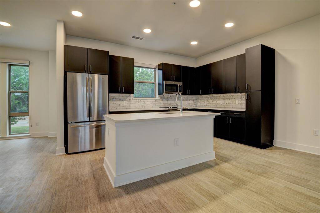 A bright kitchen featuring all stainless steel appliances and quartz countertops, complemented by a decorative backsplash.