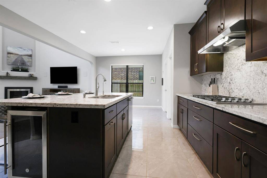 Another view of the kitchen featuring galaxy white granite countertops, extended backsplash and wine/beverage fridge.
