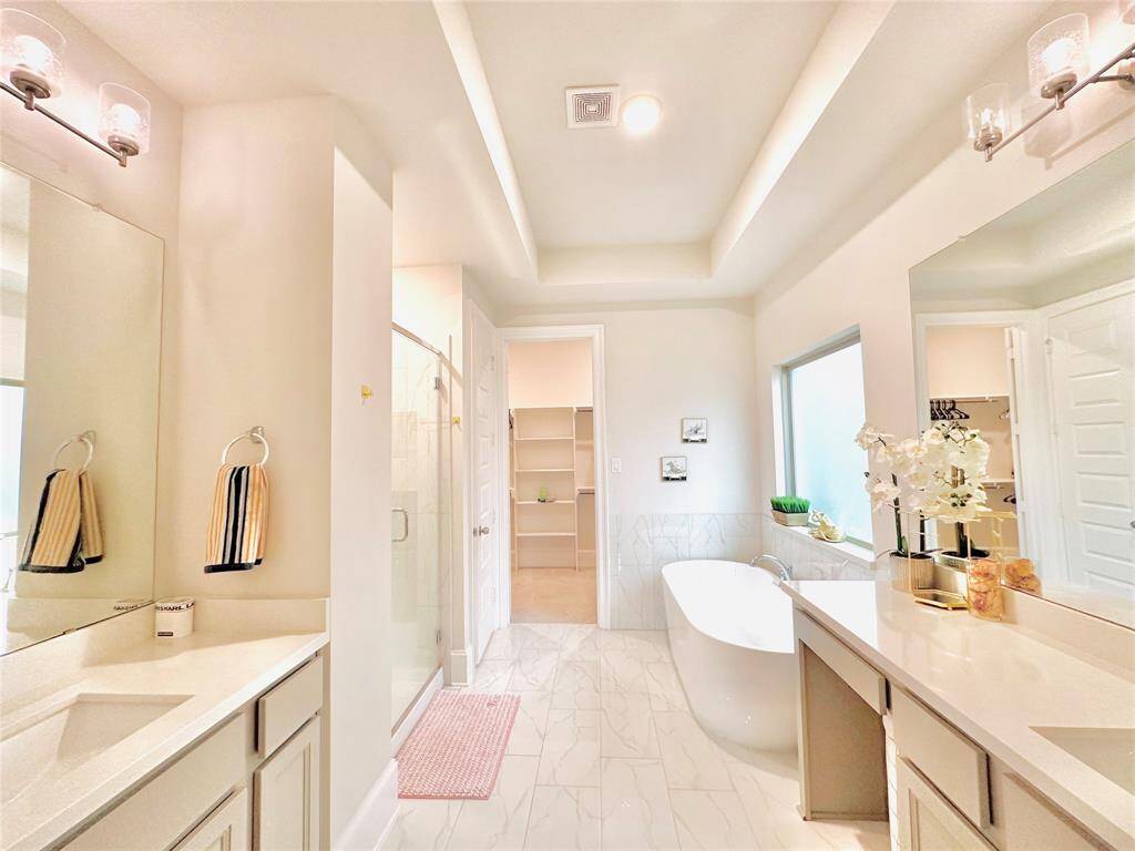 Modern bathroom featuring dual vanities, a large mirror, a freestanding tub, a separate glass-enclosed shower, and a walk-in closet. The space is finished with clean lines and a neutral color palette.