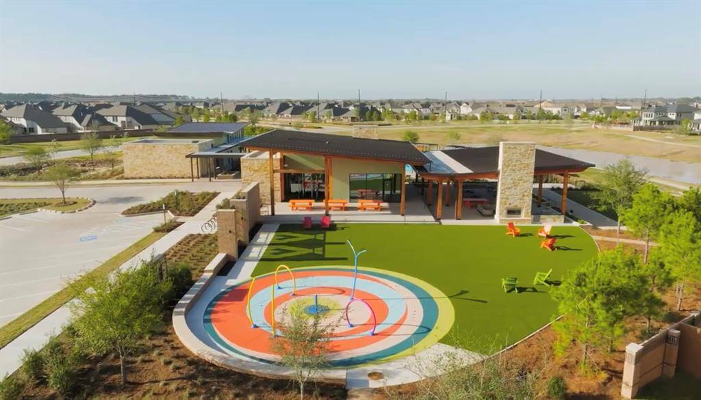 Community center with a colorful playground and ample parking, situated in a new suburban development with a variety of homes in the background. The center offers a welcoming space for residents to gather and play.