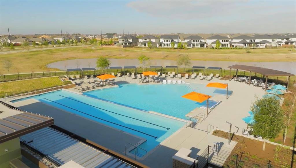 Community pool area with ample lounging space, surrounded by a scenic neighborhood of modern homes. The area includes a large pool, shaded seating, and a relaxed outdoor environment.