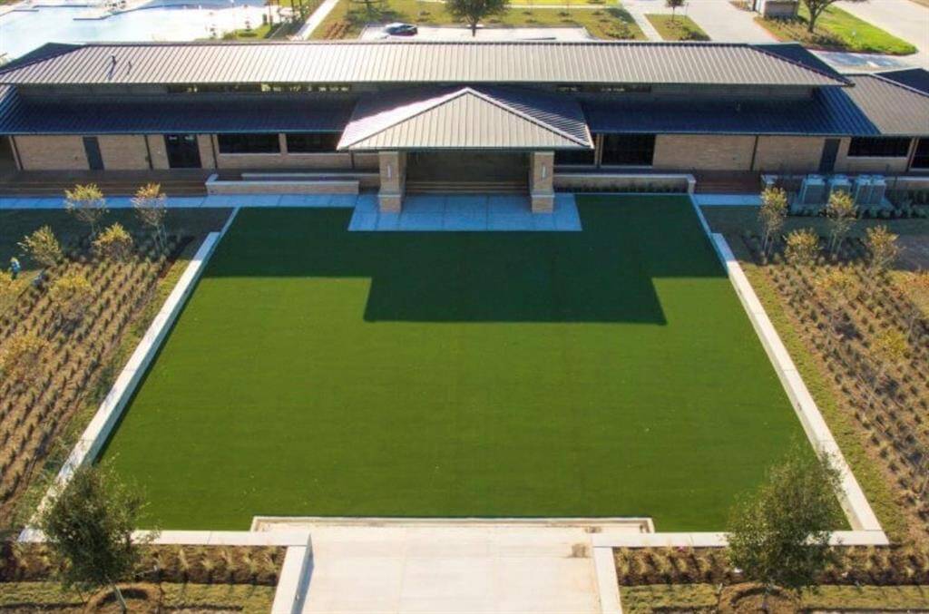 Artificial turf lawn, neatly bordered by landscaping. The building features a symmetrical design with a prominent central entrance, flanked by windows and extended roofing. The green space offers ample room for outdoor activities or future customization.