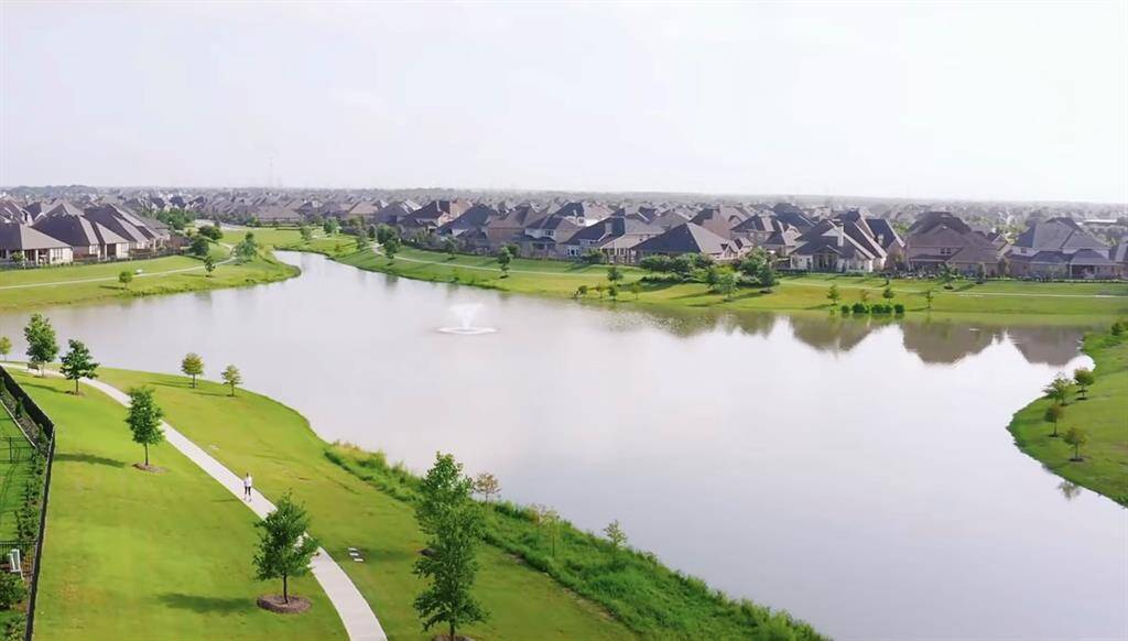 Serene suburban setting featuring spacious, modern homes alongside a beautiful lake with walking paths and green spaces, ideal for those seeking a tranquil lifestyle with outdoor amenities.