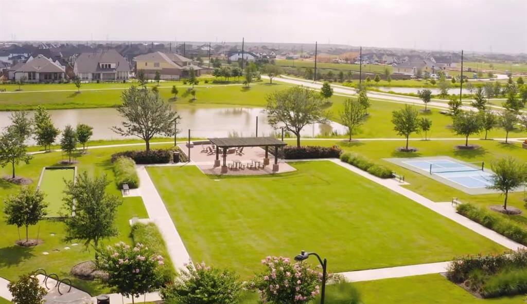 Community space featuring a pond, a gazebo with picnic seating, walking paths, neatly trimmed lawns, and a tennis court, all within a residential area.