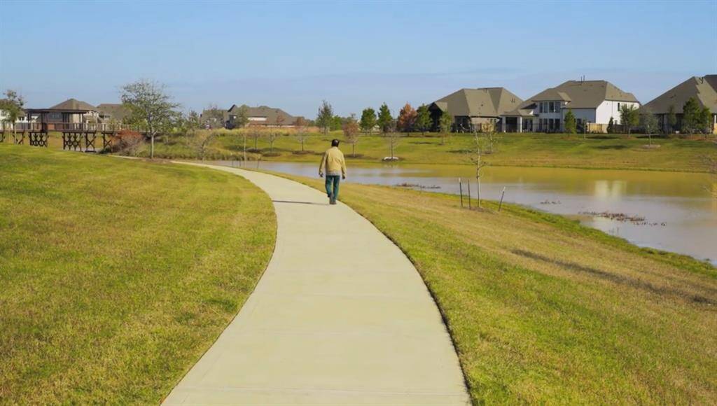 Peaceful residential area with spacious, modern homes overlooking a scenic pond, complete with a winding pathway for leisurely walks.