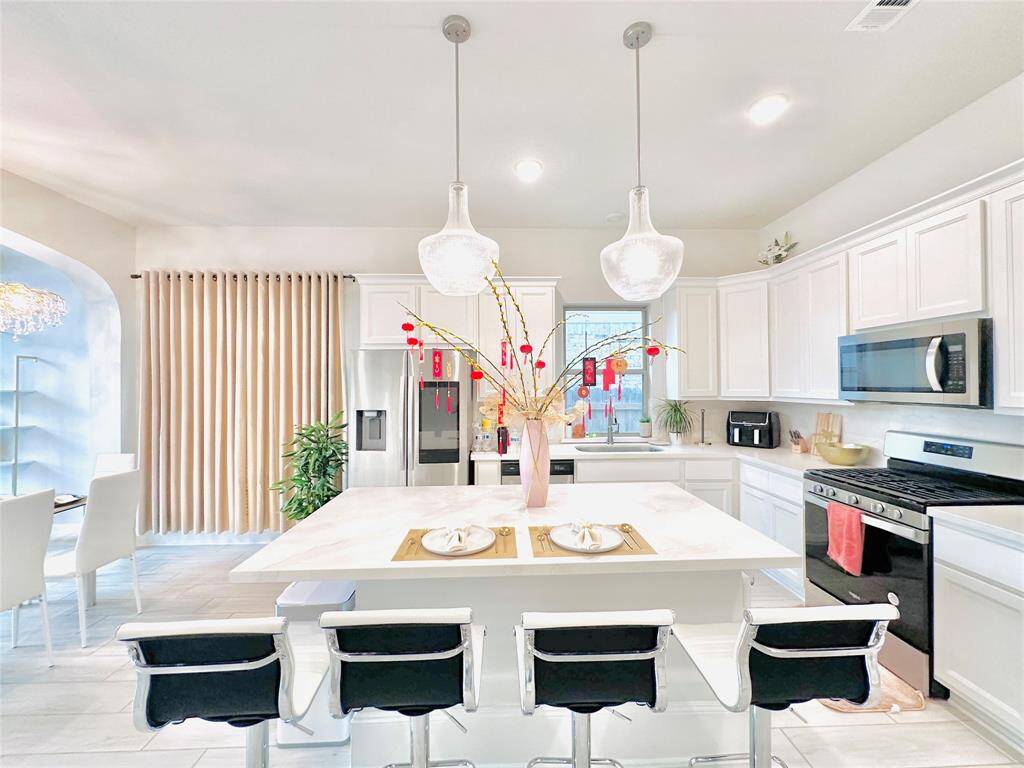 Modern kitchen with white cabinetry, stainless steel appliances, and a central island with bar seating under pendant lighting. The space is complemented by large windows and a clean, contemporary design.