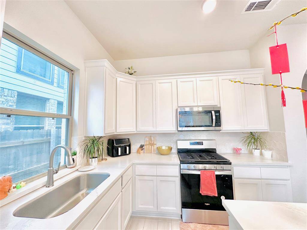 Kitchen with white cabinetry, stainless steel appliances, and a window above the sink providing natural light.