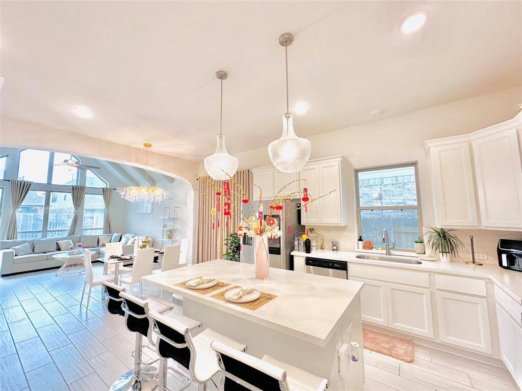 Open-concept kitchen with white cabinetry and a central island with seating, leading into a bright living area with ample natural light. Stylish pendant lights add a touch of elegance to the space.
