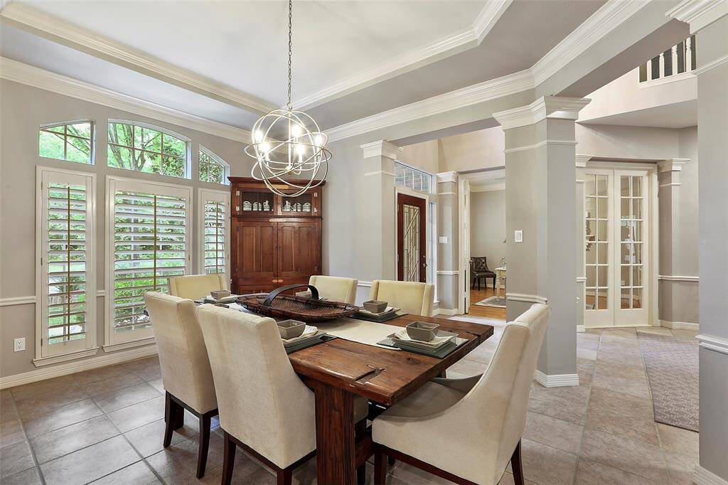 The formal dining room overlooks the mature landscape. Plantation shutters, tray ceiling with extensive crown molding, and another beautiful chandelier make this room special.