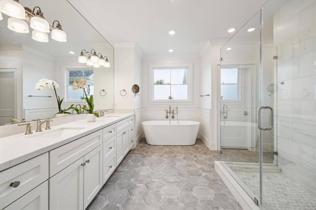 The spa-inspired primary bath showcases a large walk-in shower, freestanding soaking tub, double sinks and modern concrete hex tile.
