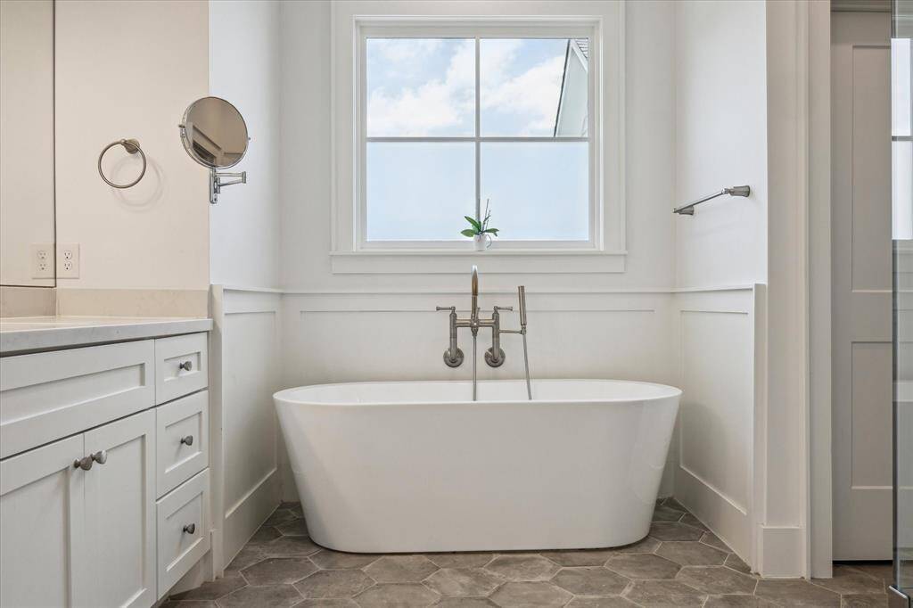 A freestanding soaking tub sits beneath a sunlit window offering a peaceful place to unwind after a long day.