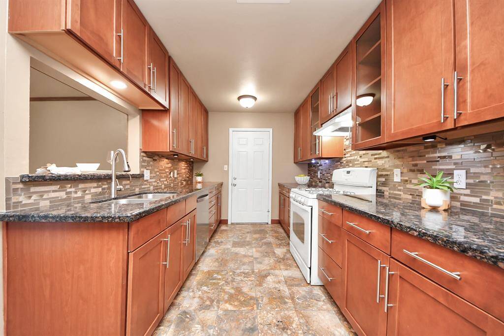 This beautifully updated kitchen features rich wood cabinetry with sleek modern hardware and granite countertops that offer both style and durability. A stunning mosaic tile backsplash adds a contemporary touch, while under-cabinet lighting enhances both function and ambiance. The galley layout provides efficient workflow, abundant storage, and ample counter space. Includes a gas range, stainless steel dishwasher, and a convenient pass-through window to the living area.