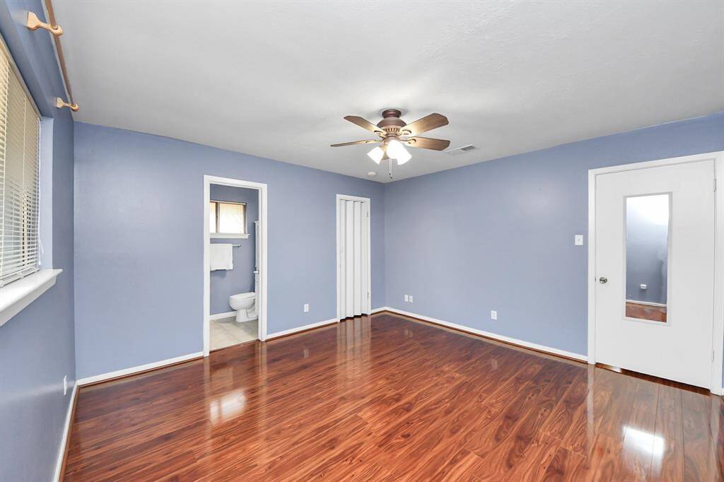 The spacious primary bedroom offers a peaceful retreat with rich wood-style flooring, soft blue walls, and plenty of natural light. A large walk-in closet provides ample storage space, making organization a breeze.