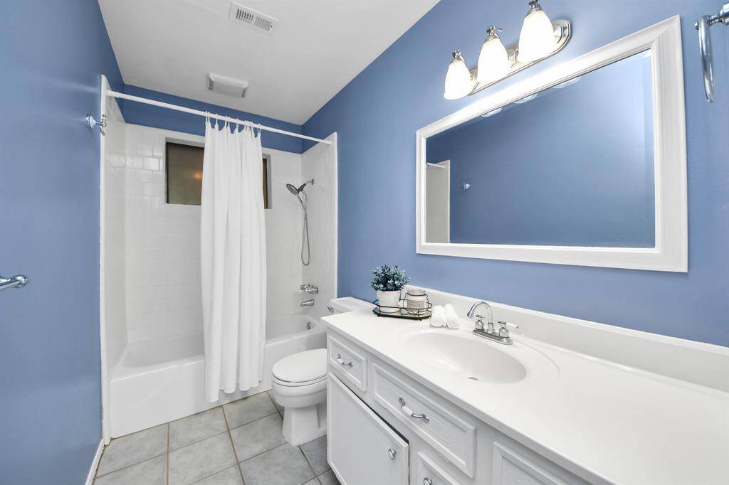 This bathroom features a tub/shower combo with classic tile surround, a spacious vanity with storage, and soft blue walls for a fresh, calming feel.