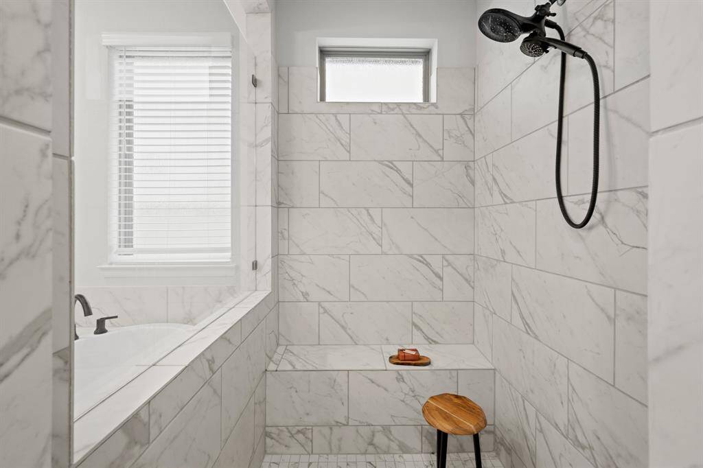 The primary bath features a huge walk in shower, complete with sleek plumbing fixtures, mud set tile floors, a bench, and window to let in natural light.