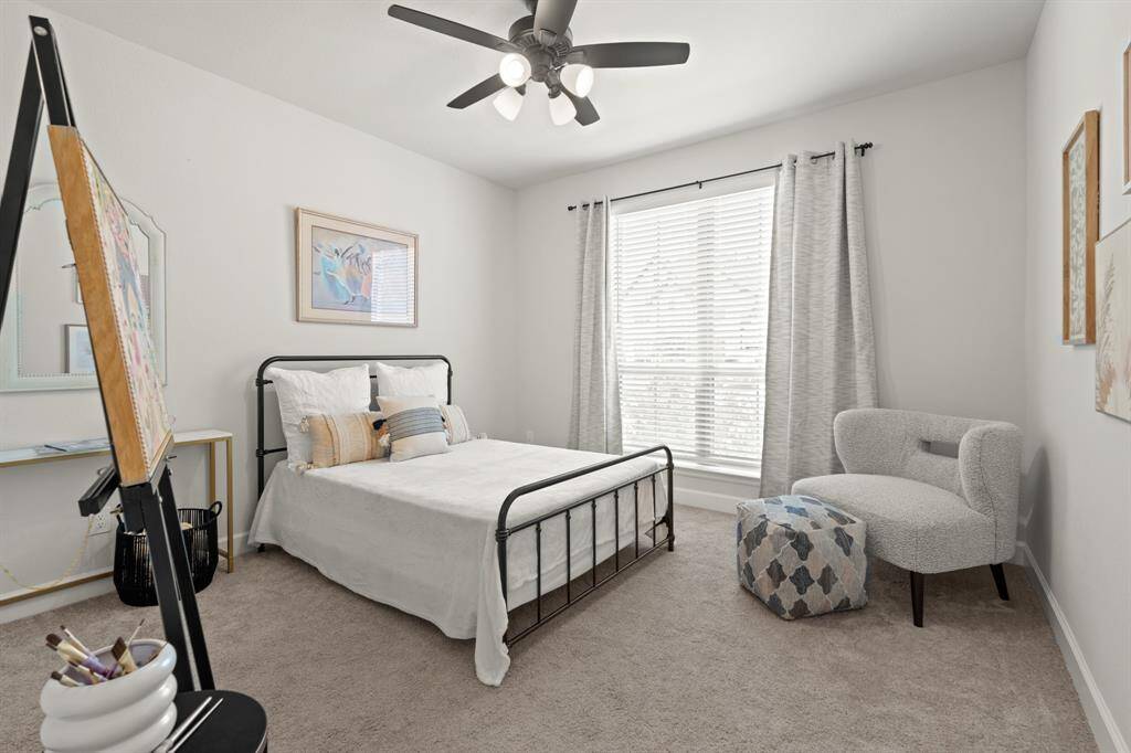 Located at the front of the home is the second downstairs bedroom with private full bathroom. It features plush carpet, neutral paint, a ceiling fan, and large windows letting in bright natural light.