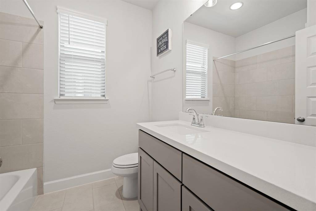 This full bathroom is located off the hall of the secondary bedrooms making it easy to share and get ready. It features a large vanity, gray cabinets, quartz countertops, and a combined shower and tub.