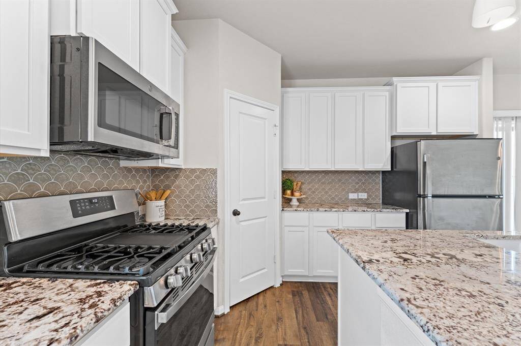 Stainless steel appliances, a stylish tile backsplash, and pristine white custom cabinets add a modern touch.