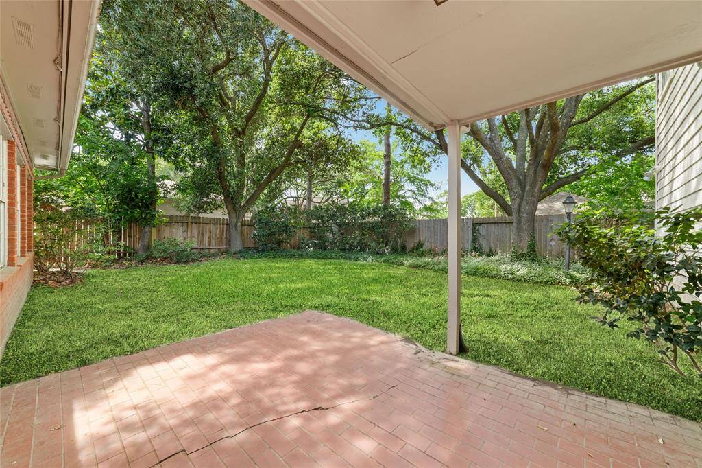 Pretty covered brick patio looking onto the shaded back yard.
