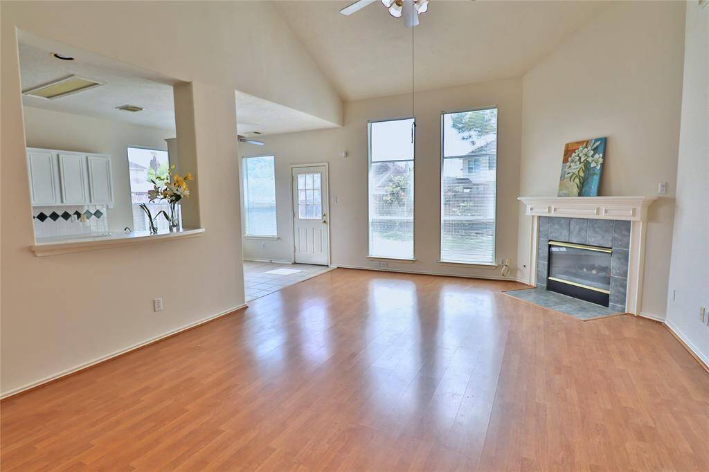 This spacious family room features high ceiling, wood flooring, large windows for natural light, and a cozy fireplace.