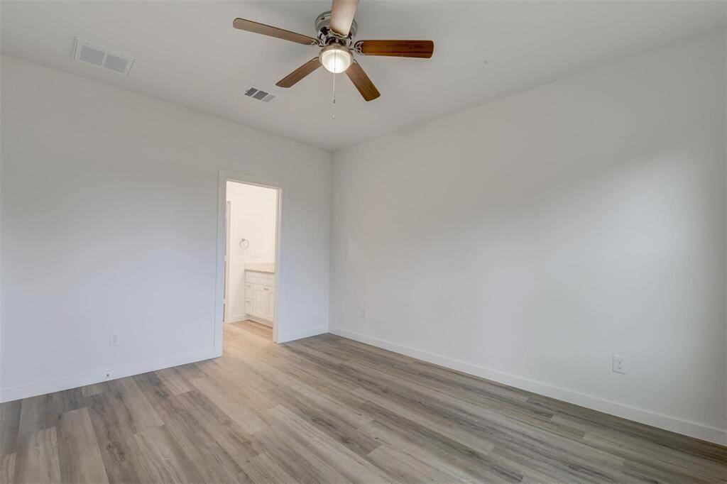 This modern room features light vinyl wood flooring, neutral walls, and a ceiling fan, seamlessly connecting to a convenient bathroom.