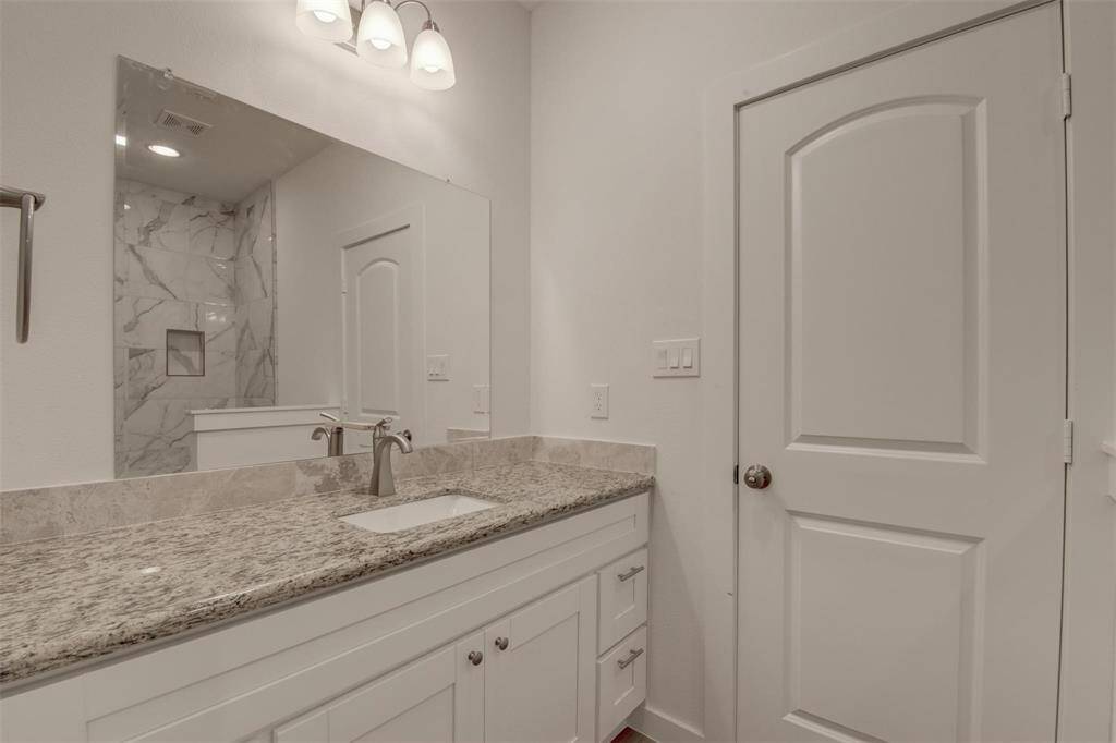 Experience modern elegance in this bathroom with a granite countertop, under-mount sink, and white cabinetry. Enjoy the large mirror, recessed lighting, and easy access to a tiled shower area.