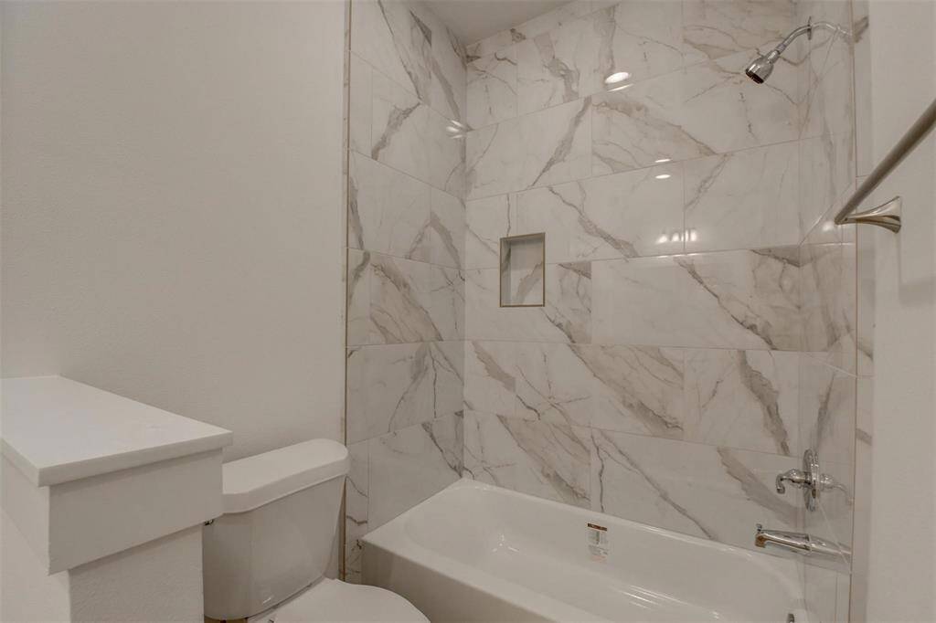 Discover modern elegance in this bathroom featuring a sleek white tub and toilet, accented by marble-patterned tiles and a built-in shower niche.