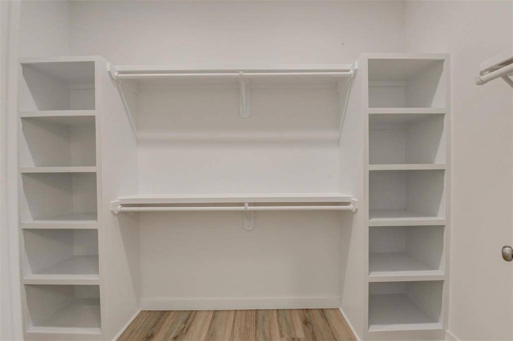 Experience organized elegance in this spacious walk-in closet, featuring open shelves and dual hanging rods against light-colored walls and flooring. Perfect for maximizing storage.
