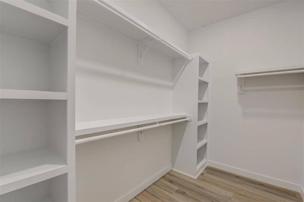 Discover a bright, spacious walk-in closet with built-in shelves and hanging rods, featuring sleek, light vinyl wood flooring for a modern touch. Ideal for ample storage.