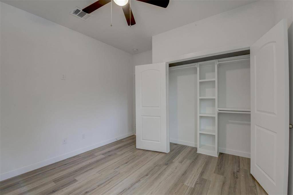 Experience modern elegance with light vinyl wood flooring, neutral walls, a ceiling fan, and a spacious closet featuring built-in shelves for ample storage.