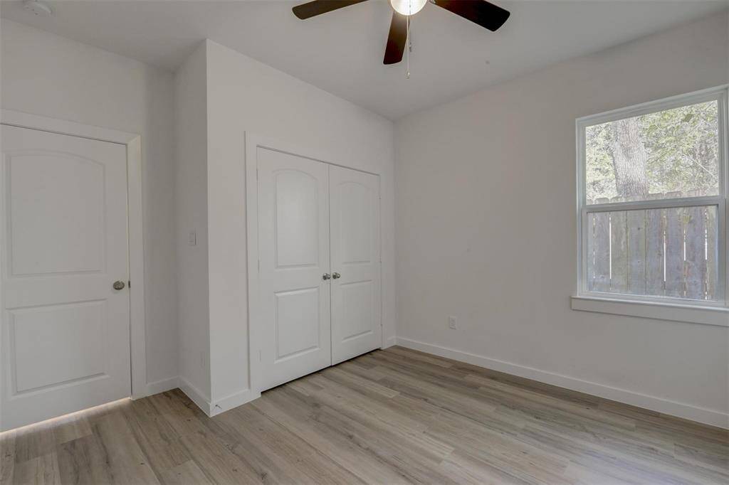 This bright room features light vinyl wood flooring, a ceiling fan, and a large window providing natural light. It includes a closet with double doors, ideal for storage. Perfect as a bedroom or home office.
