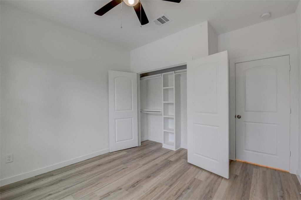 Bright room with light vinyl wood flooring, a ceiling fan, and a spacious white closet with built-in shelving. Perfect for a bedroom or office.