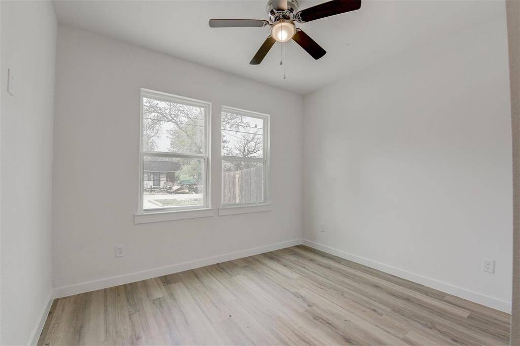 Bright and versatile room featuring light vinyl wood flooring, two large windows, a ceiling fan, and neutral walls—ideal for a bedroom or office.