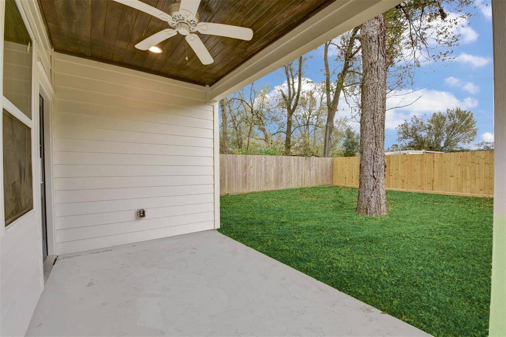 A cozy patio with a ceiling fan opens to a private, fenced backyard with mature trees for a serene outdoor retreat.