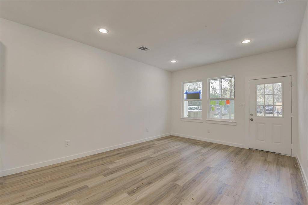 This photo shows a bright, open living space with light vinyl wood flooring, white walls, recessed lighting, and a door with adjacent windows letting in natural light. Perfect for a cozy and modern setup.